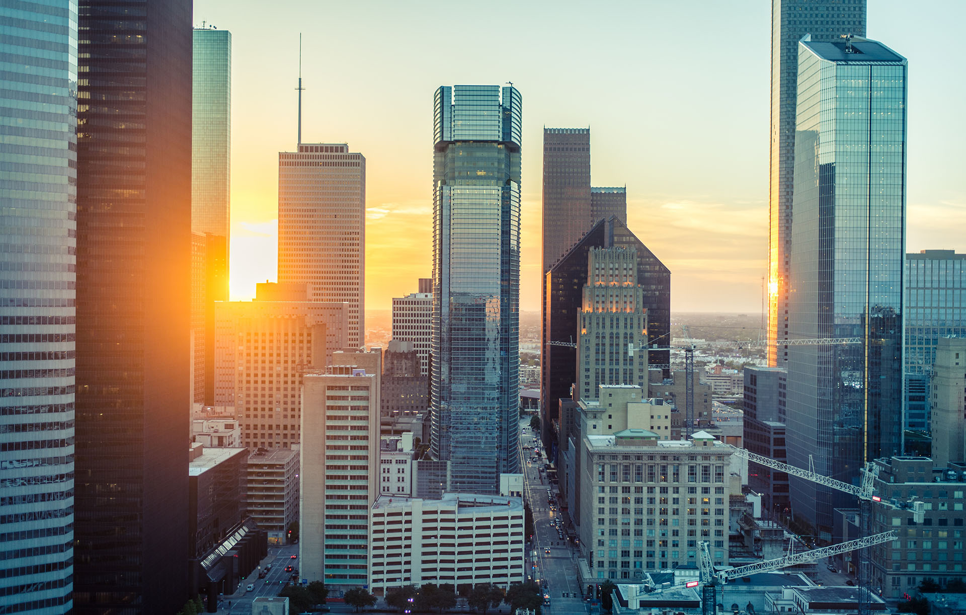 An orange-glowing sun setting behind the glass skyscrapers of Houston, Texas, USA